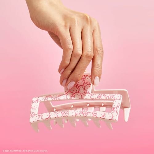 Hand holding a Hello Kitty-themed hair clip on pink background.